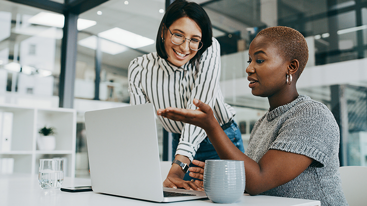 Two happy women looking at laptop in the office