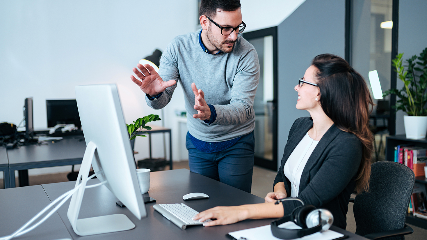 Man conversing with his smiling female coworker in front of a computer