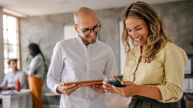 Male and female coworkers smiling while looking at mobile devices